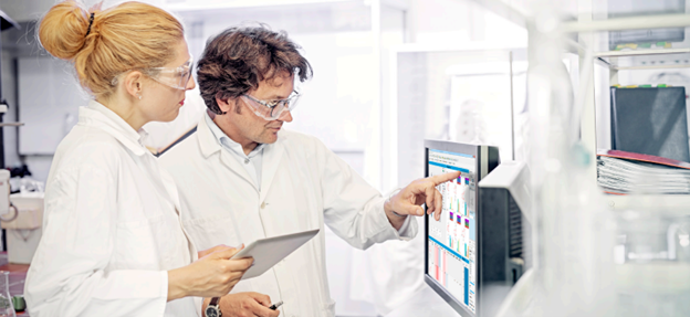 Woman with strawberry blonde hair in bun and Man with brown hair and glasses looking at Monitor