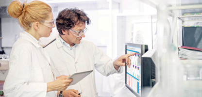 Woman with strawberry blonde hair in bun and Man with brown hair and glasses looking at Monitor