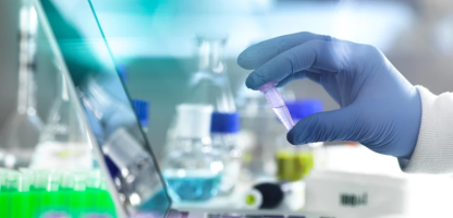 close up of laptop with persons gloved hand holding a test tube