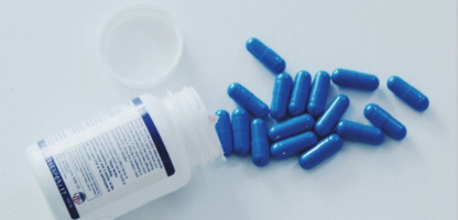 plastic white pill bottle laying by a dozen of blue capsule pills 