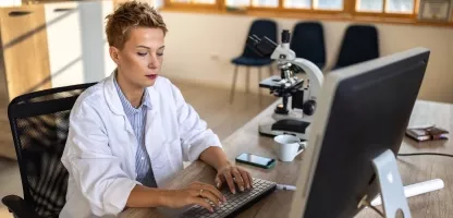 A woman scientist in a white coat typing on a computer