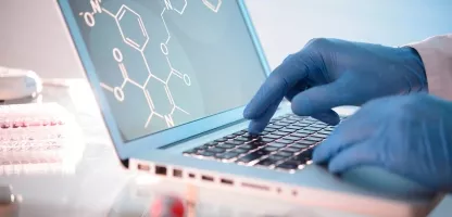 A person wearing blue gloves typing on a laptop with chemistry characters displayed on the screen