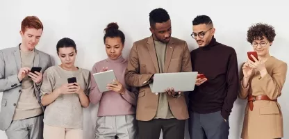 A group of young adults standing in a horizontal line looking at an electronic device
