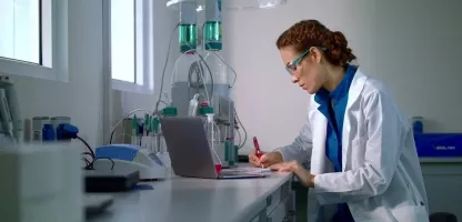 Woman scientist in a white coat with glasses on writing on a notebook in a scientific lab