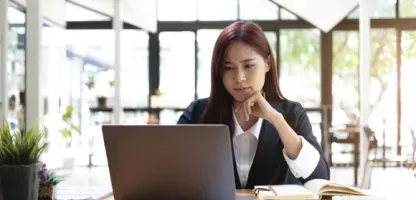 lady with dark brown hair looking at laptop screen in office setting