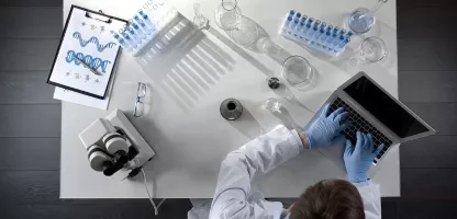 A top down view of a scientist working on a laptop with scientific equipment placed neatly around on the workbench