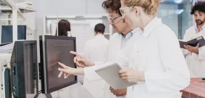 Scientists in white coats pointing at computer monitors