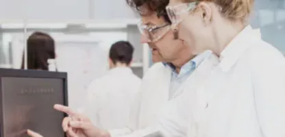 Two scientists looking at computer screen monitor w/ Scientist in the background